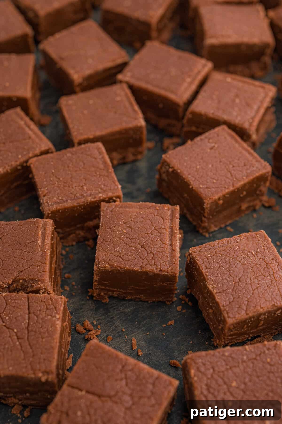Homemade chocolate fudge squares arranged on a dark surface.