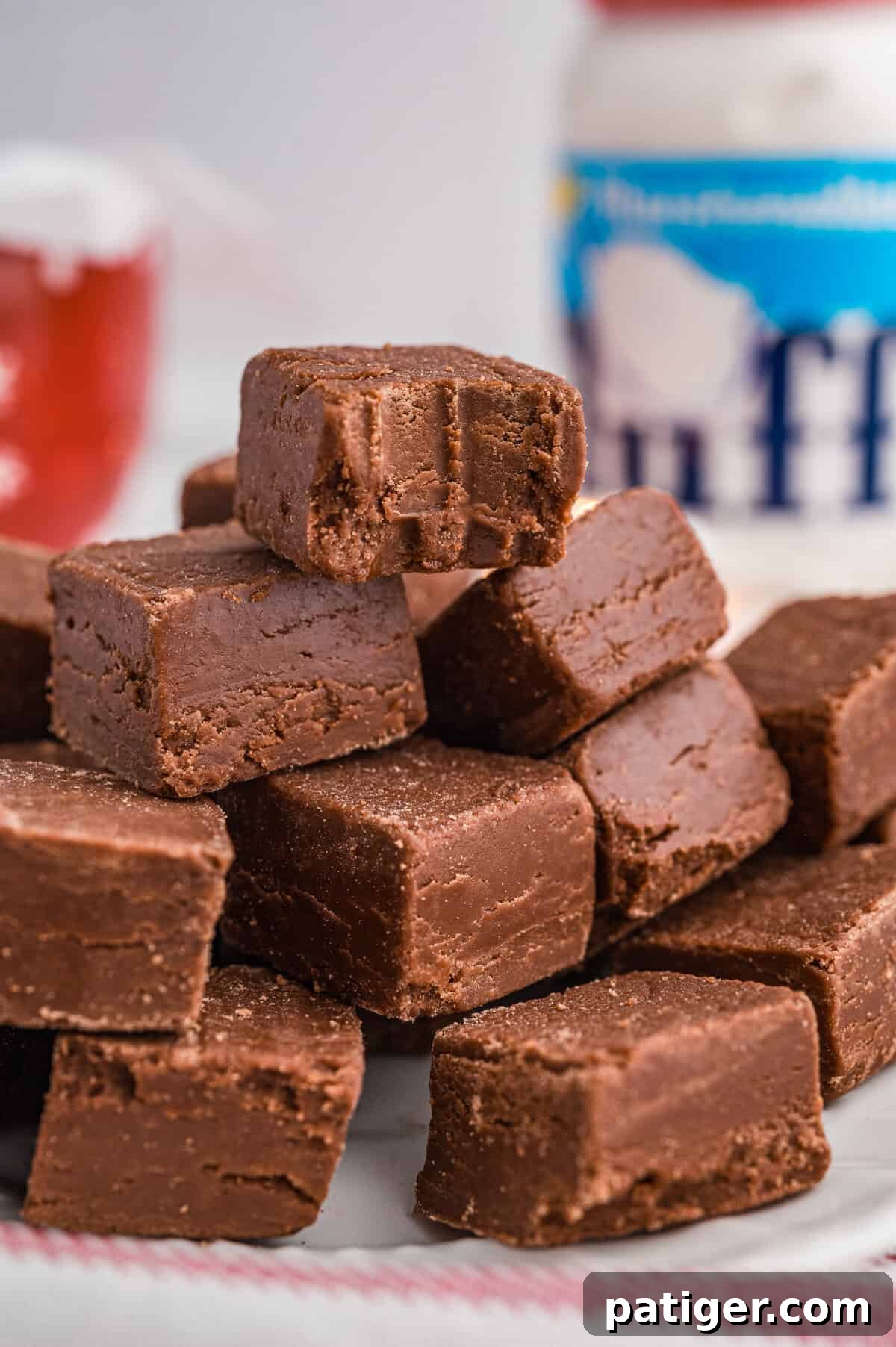 A bitten chocolate fudge made with marshmallow fluff stacked on top of other pieces with a jar of Marshmallow Fluff in the background.