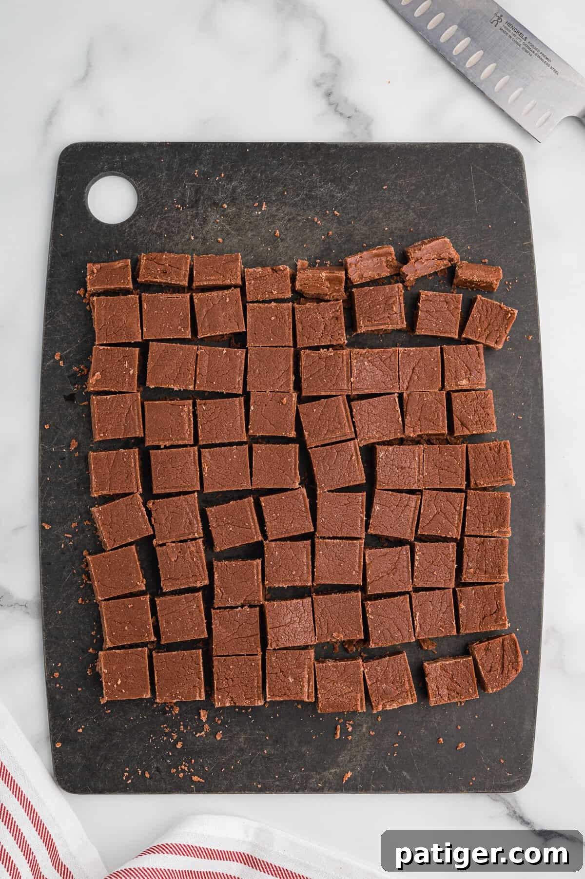 Overhead view of neatly cut never fail fudge squares arranged on a dark cutting board.