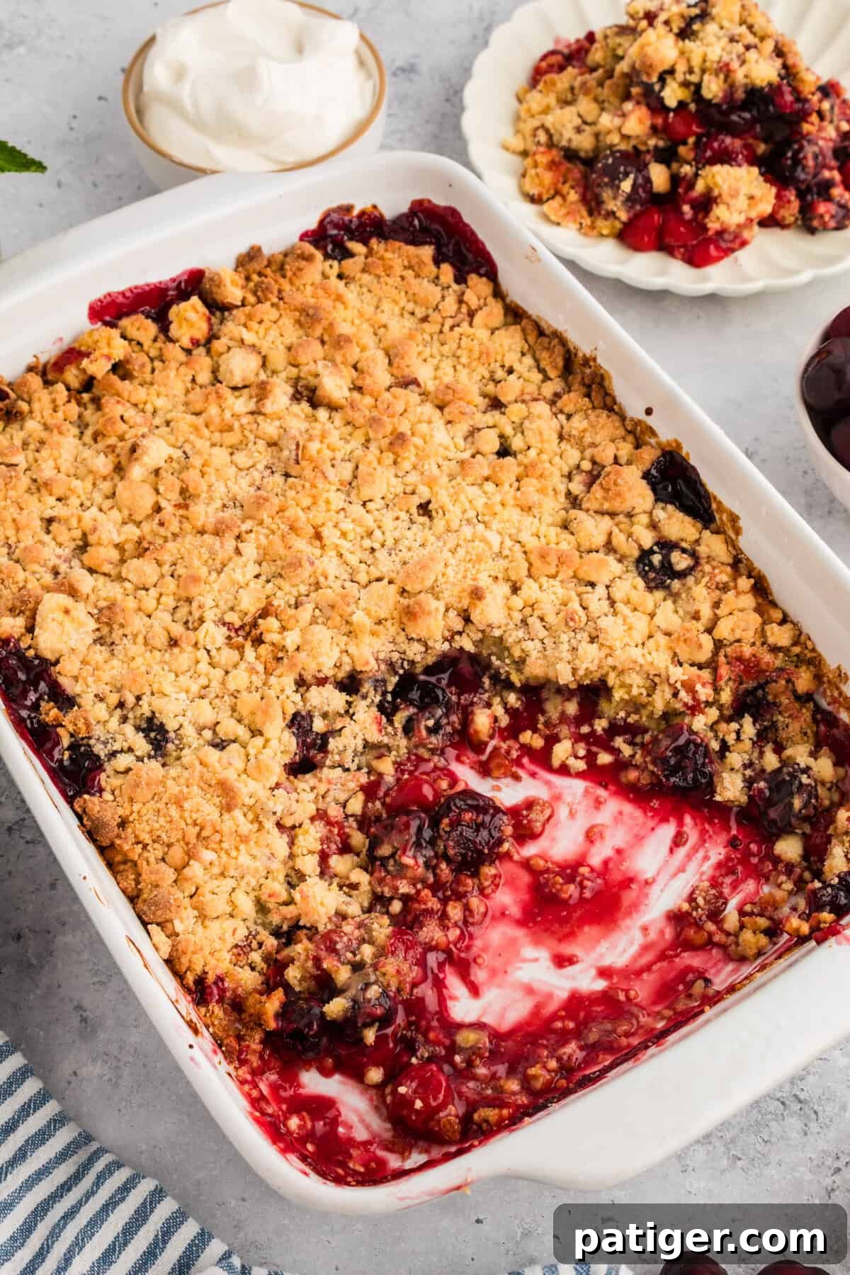 Baked cherry cobbler with yellow cake mix in a white rectangular dish, showing a golden crumbly topping and a missing portion revealing cherry filling. Served warm and ready to eat.