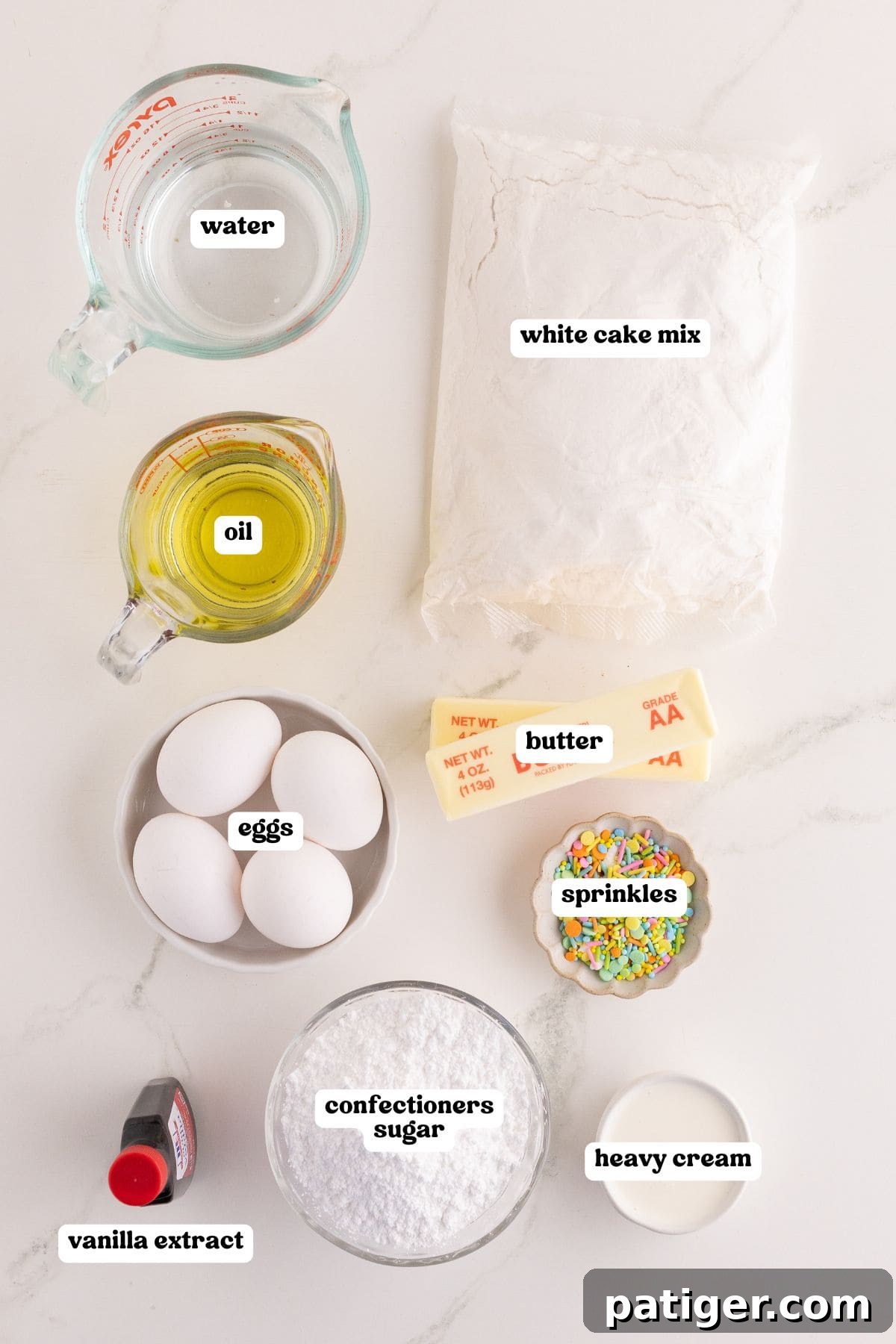 Charming Easter Bunny Cake 3 Ingredients for bunny cake labeled: water, oil, a bag of white cake mix, eggs, butter, pastel sprinkles, confectioners sugar, heavy cream, and vanilla extract.