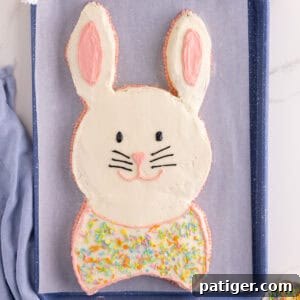 Easter bunny cake with white frosting and pink ear details, piped face, and bow tie.