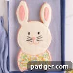 Easter bunny cake with white frosting and pink ear details, piped face, and bow tie.