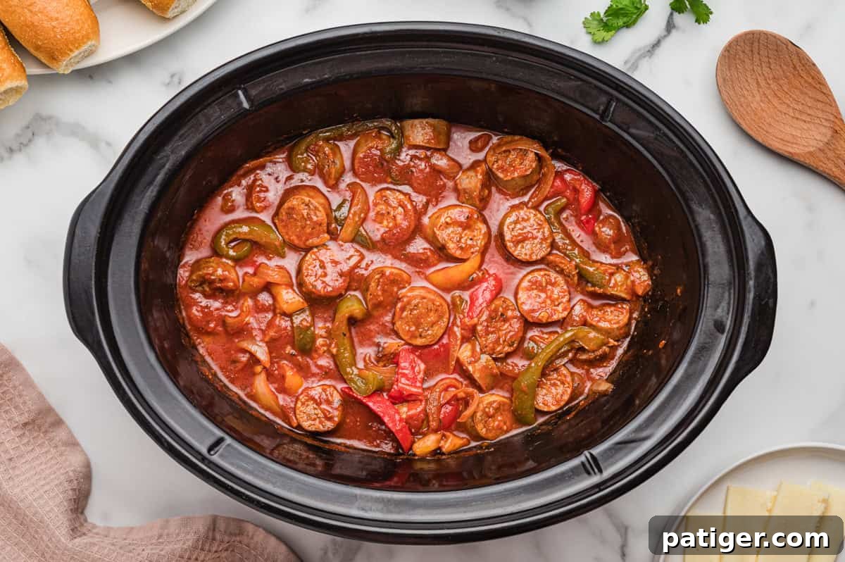 Top-down view of sausage and peppers in sauce inside a slow cooker.