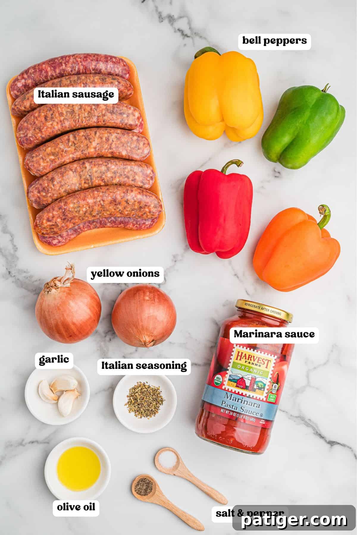 Ingredients for sausage and peppers laid out on a marble surface with labels: a pack of raw Italian sausages, yellow, green, red, and orange bell peppers, two yellow onions, garlic cloves, Italian seasoning, a jar of marinara sauce, a small dish of olive oil, and wooden spoons holding salt and pepper.