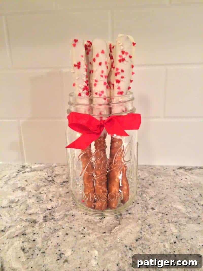 Beautifully arranged white chocolate dipped Valentine's Day pretzel rods, garnished with vibrant heart sprinkles, perfect for a romantic gesture or sweet snack.