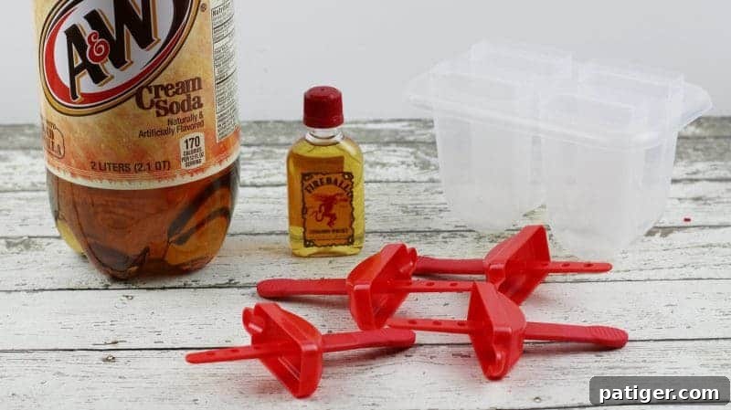 A two-liter bottle of A&W Cream Soda, a small airplane-sized bottle of Fireball Whiskey, and a four-cavity ice pop mold laid out on a surface, clearly showing the minimal ingredients and equipment needed for this easy recipe.