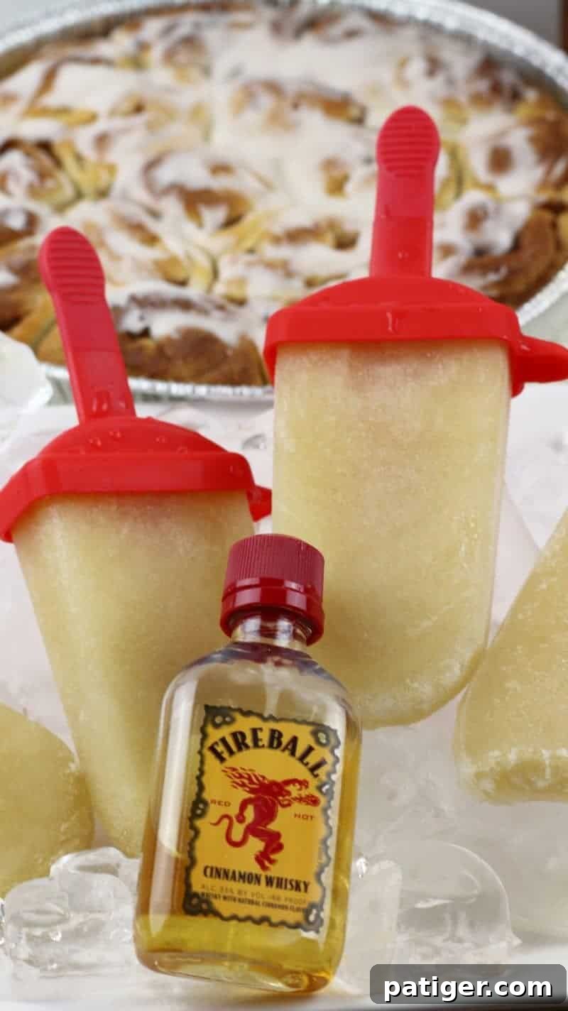 A vibrant platter of Fireball Whiskey cinnamon roll ice pops on ice, with a tray of cinnamon buns and a bottle of Fireball cinnamon whiskey in the background. This image highlights the dessert's inspiration and serving suggestions.