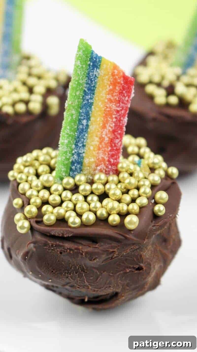 A close-up shot of a single Pot of Gold Oreo truffle, exquisitely decorated with an arching rainbow candy and sparkling gold balls on top.