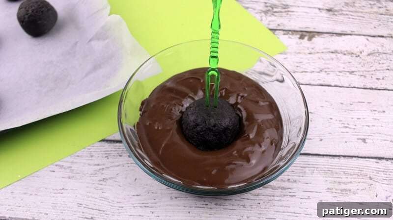 An Oreo truffle ball being carefully dipped into a bowl of melted chocolate using a toothpick, ensuring an even coating.