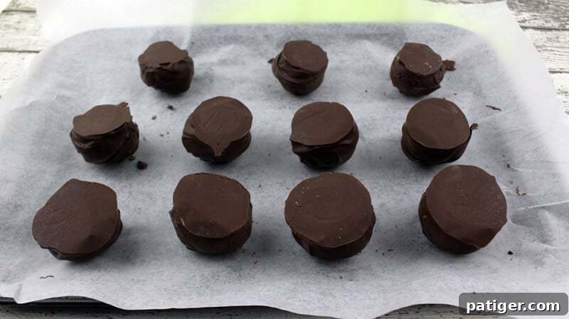 Chocolate-covered Oreo balls flipped upside down on a lined baking sheet, creating a flat surface for decoration.