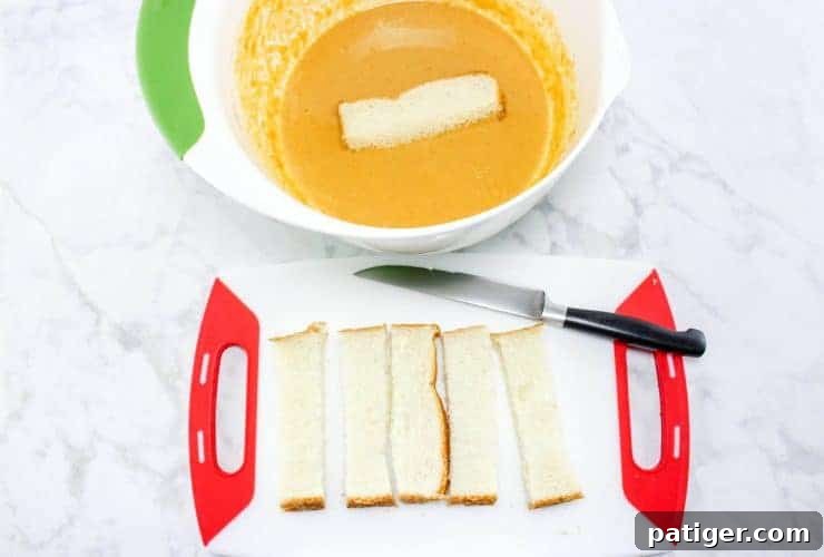 Bread and knife on cutting board. Bread is cut into thick strips and one strip is placed in pumpkin batter. 