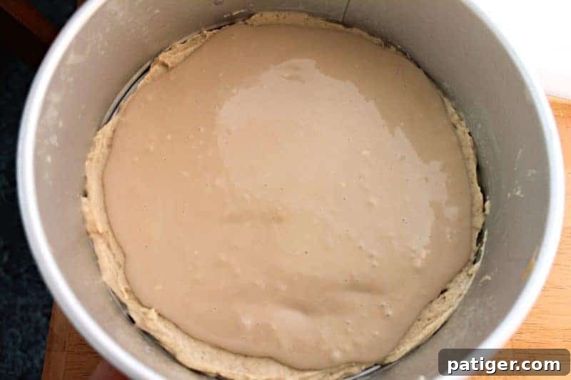 Cream cheese filling being poured over the first layer of coffee cake batter.
