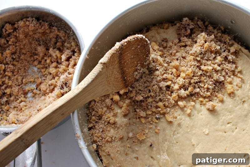 Final layer of streusel being sprinkled over the top of the assembled coffee cake before baking.