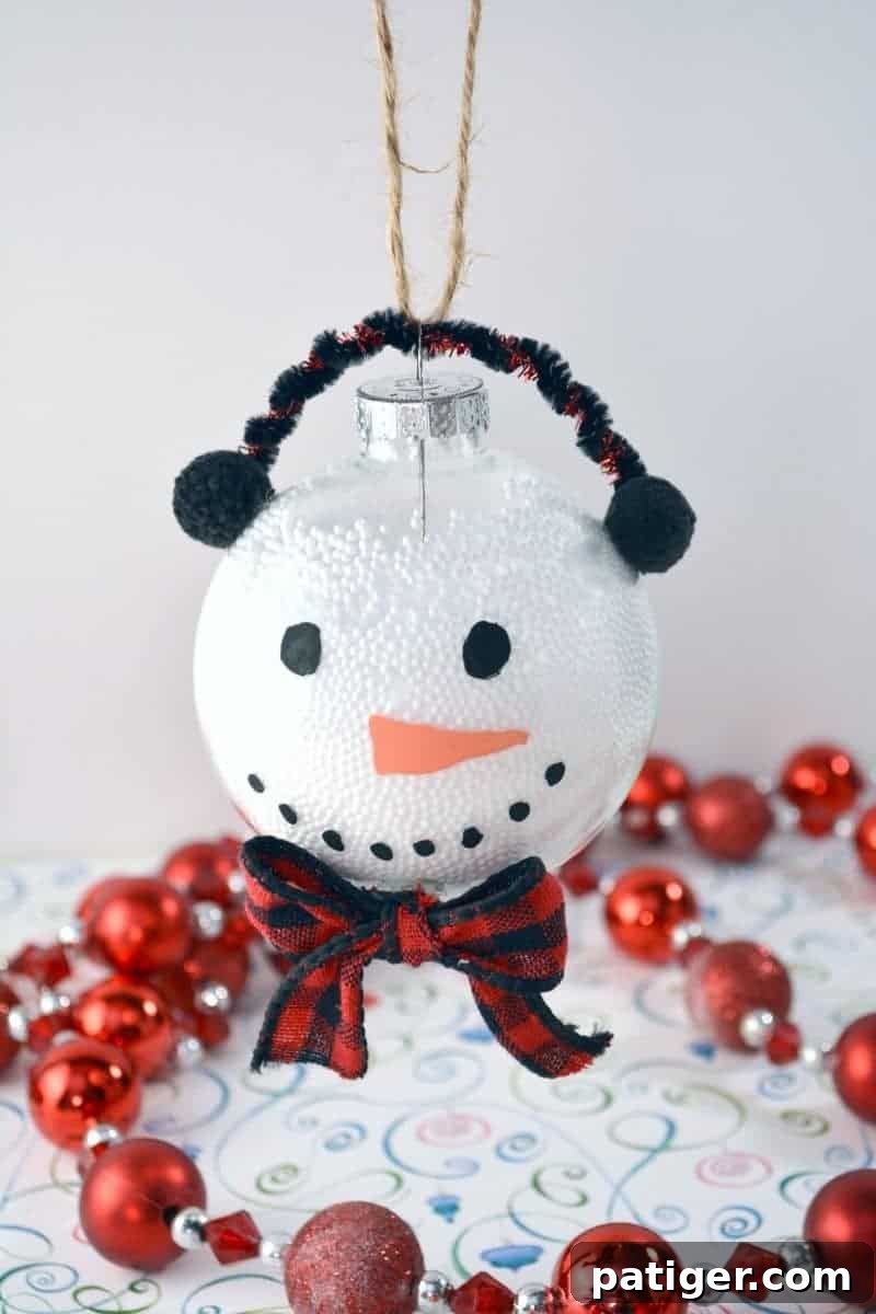 The fully completed clear Christmas ball snowman ornament, showcasing its painted face, pom-pom earmuffs, ribbon bow, and twine hanger, ready to be a cherished Christmas tree decoration.