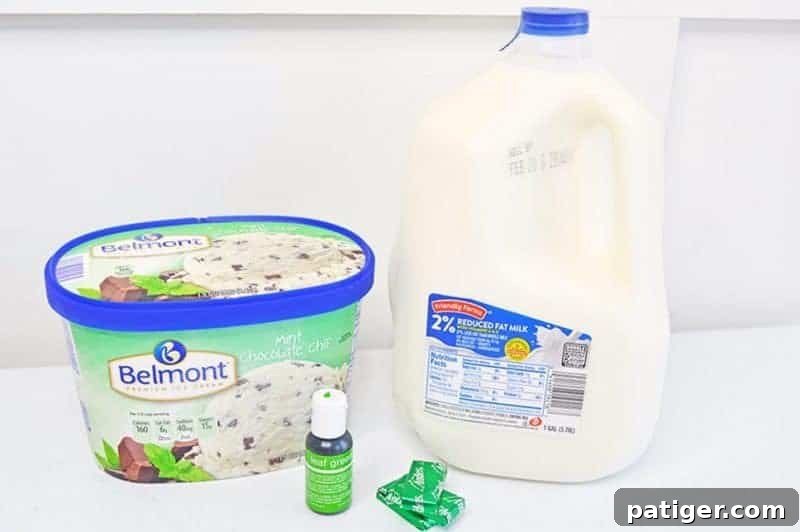 Ingredients laid out on a kitchen countertop for making a Shamrock Shake, including a half-gallon carton of mint chocolate chip ice cream, a gallon of 2% milk, a bottle of leaf green gel food coloring, and three Andes Mint candies for topping.