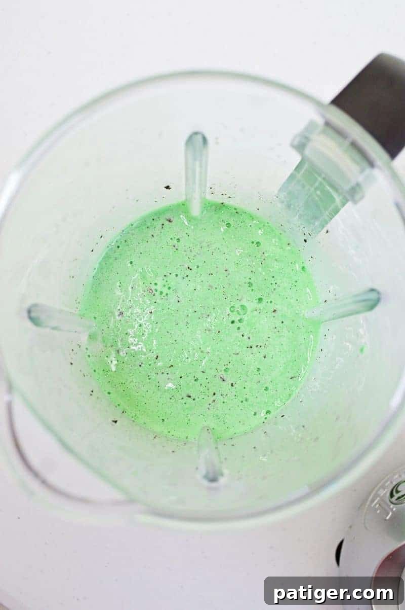 A bright green mint chocolate chip milkshake being blended in an electric blender, showing the smooth, vibrant consistency as it swirls.