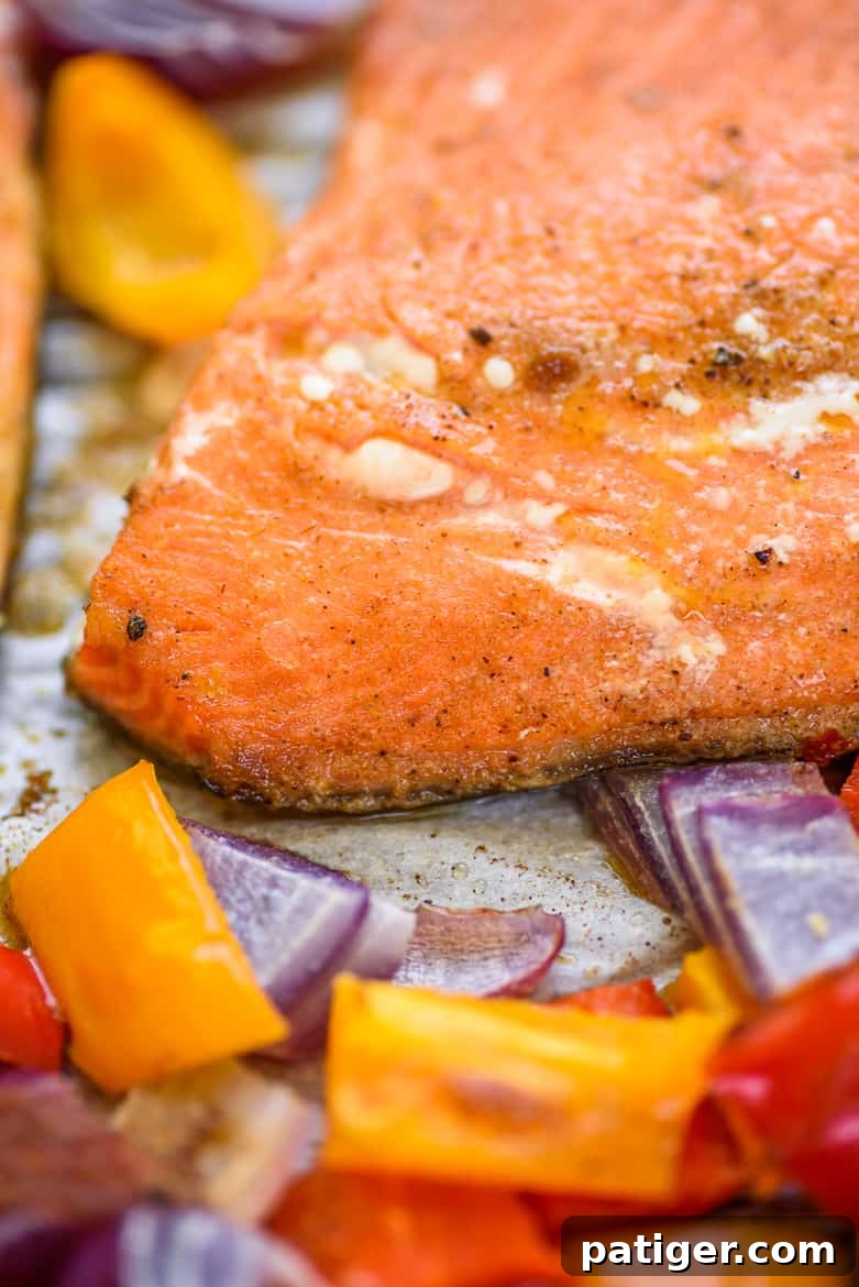 A close-up view of a chili lime salmon fillet, alongside perfectly roasted peppers and onions, still on the sheet pan, ready to be served.