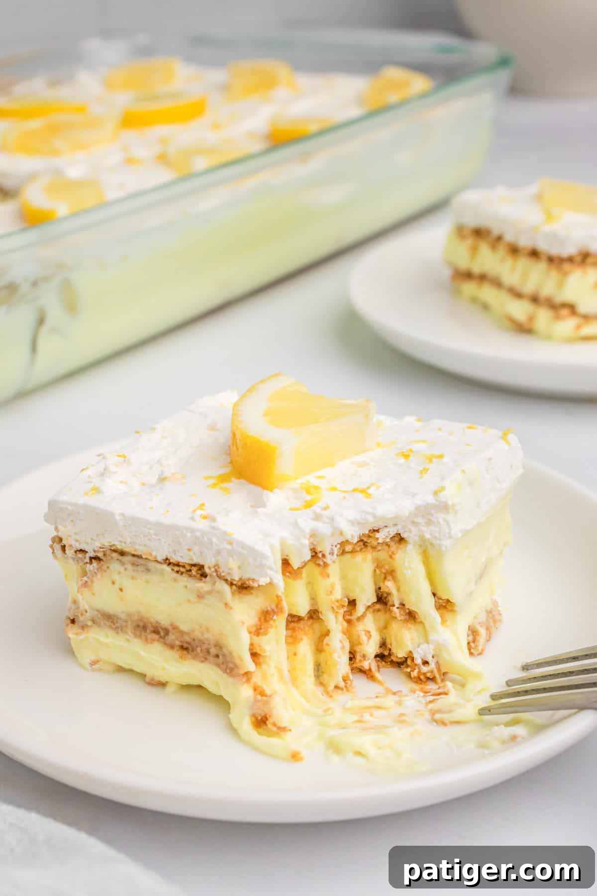 A perfectly sliced piece of lemon icebox cake with a bite taken out, revealing distinct layers of creamy lemon pudding, soft graham crackers, and airy whipped topping.