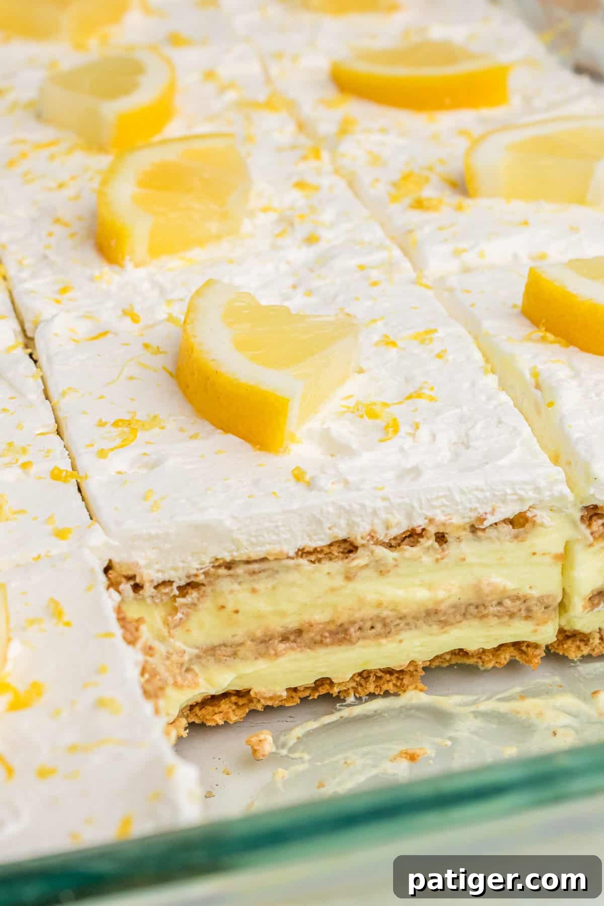 A vibrant, layered lemon dessert showcasing distinct strata of bright yellow lemon pudding, golden-brown graham crackers, and a cloud of white cool whip, ready to be served.