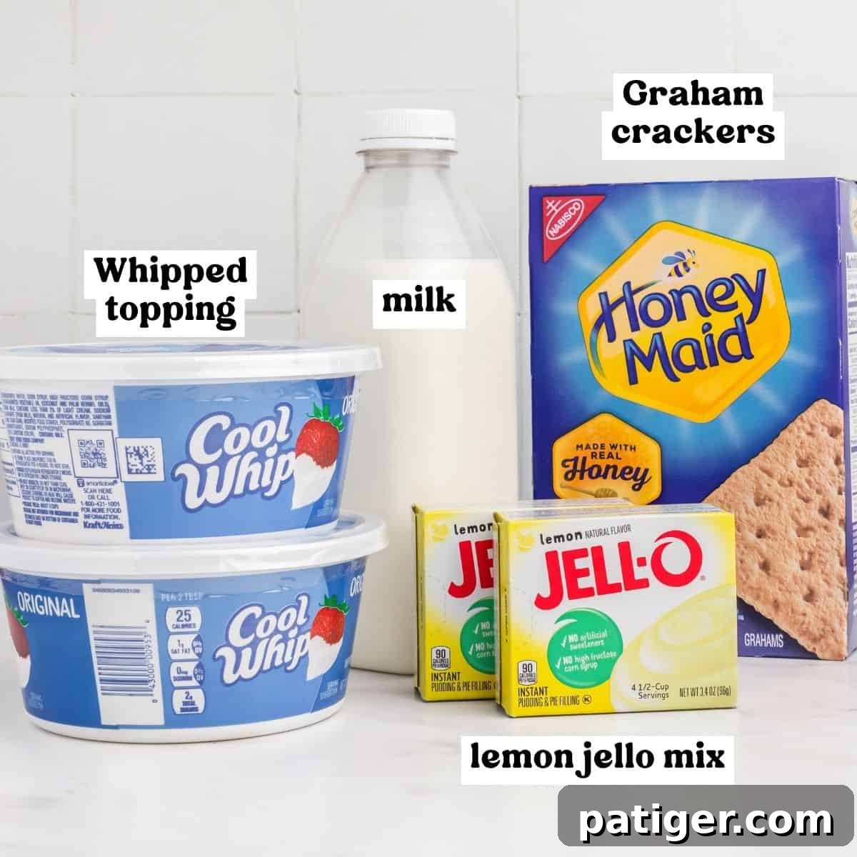 Ingredients laid out: two tubs of Cool Whip whipped topping, two boxes of lemon instant Jello mix, a stack of Honey Maid graham crackers, and a glass of milk.
