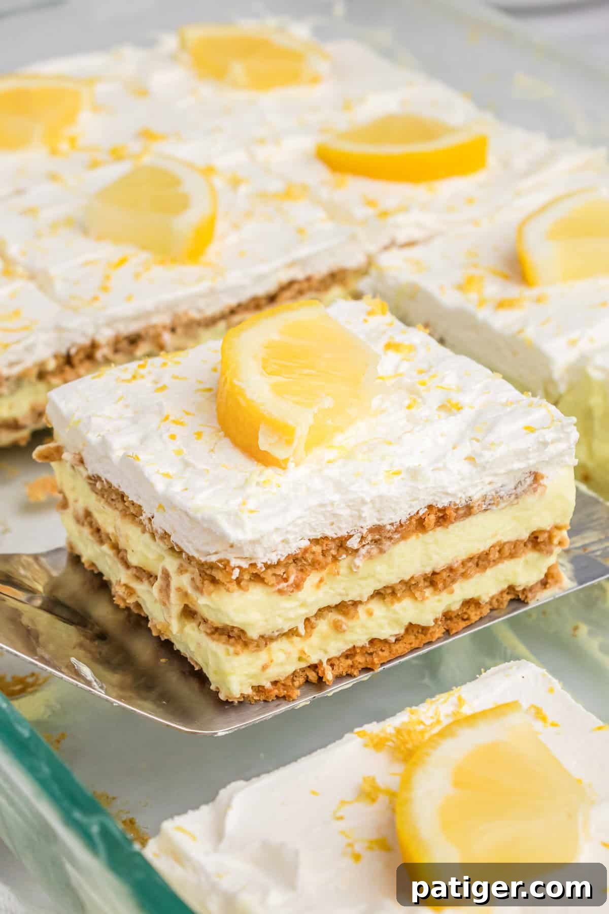 A square slice of the layered lemon pudding dessert being carefully lifted from the glass baking dish with a metal spatula, showcasing its perfectly set layers.