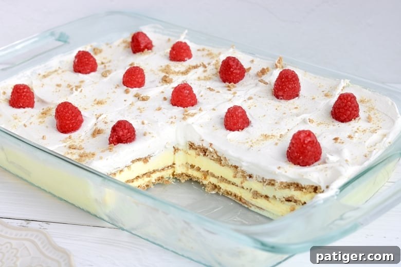 A no-bake lemon pudding cake with a few slices already removed, revealing the beautifully constructed layers of graham crackers, lemon pudding, and whipped topping. 