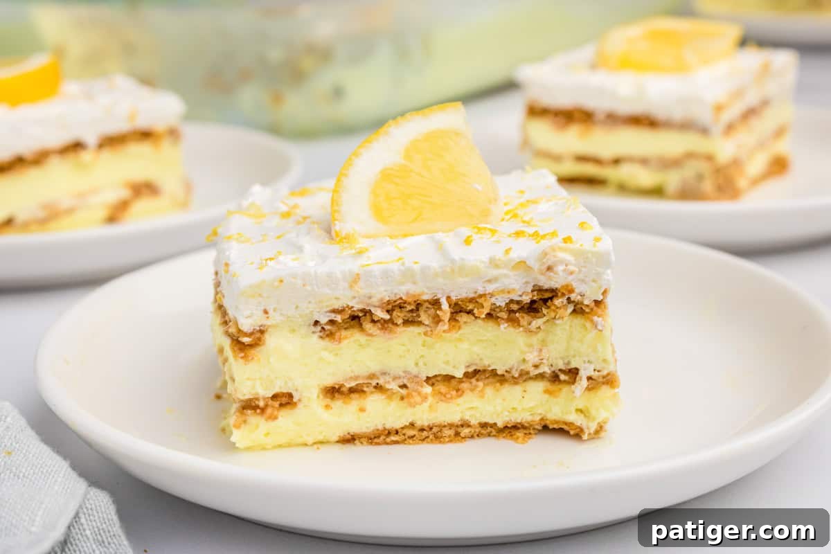 A pristine slice of icebox lemon cake, highlighting its perfectly defined layers of golden-brown graham crackers, pale yellow lemon pudding, and a generous top layer of fluffy white Cool Whip.