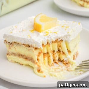 Layered lemon pudding, graham cracker, and cool whip dessert topped with a fresh lemon slice.