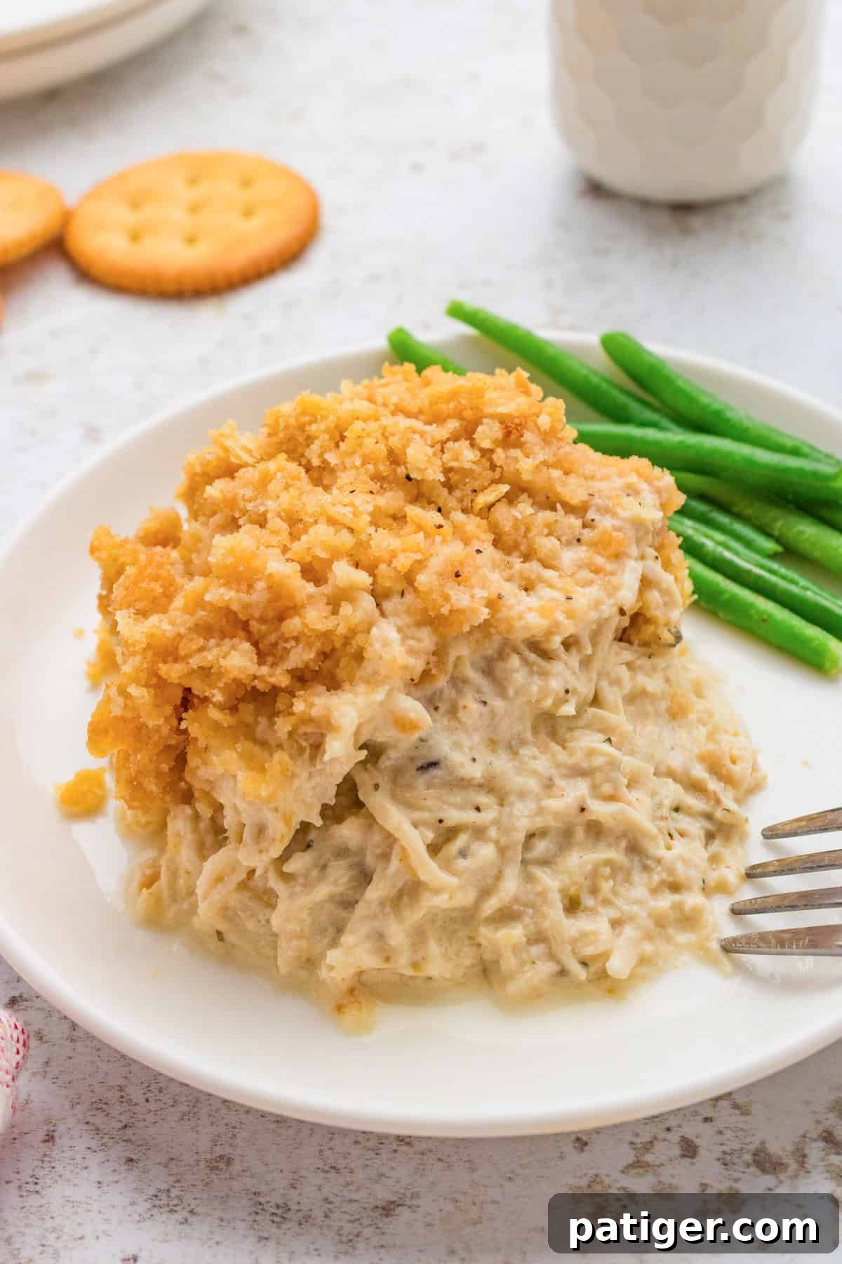 Creamy ritz chicken casserole served with green beans on white plate with ritz crackers and drink in the background.