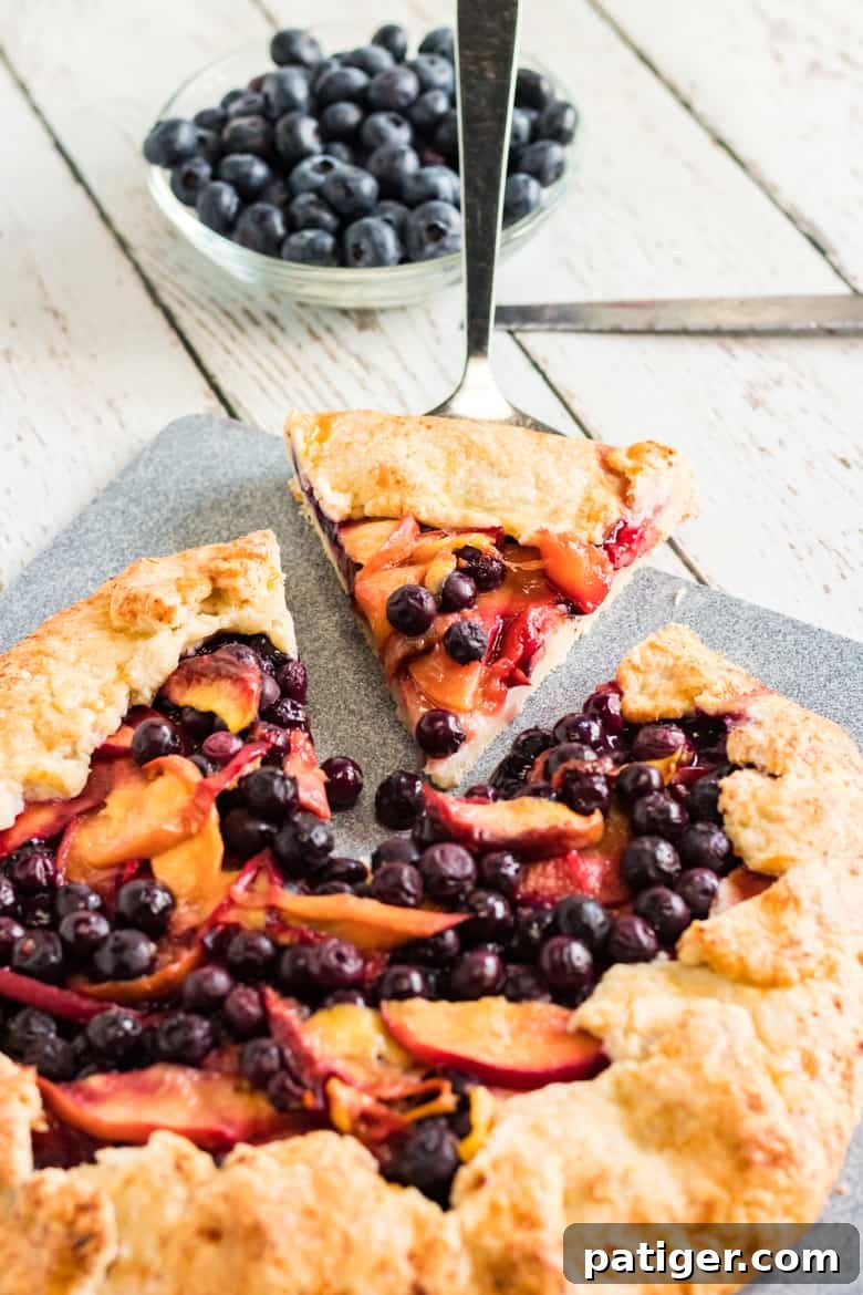 Rustic Peach Blueberry Galette with a slice being served, showcasing the warm fruit filling and golden crust, accompanied by fresh blueberries in the background.