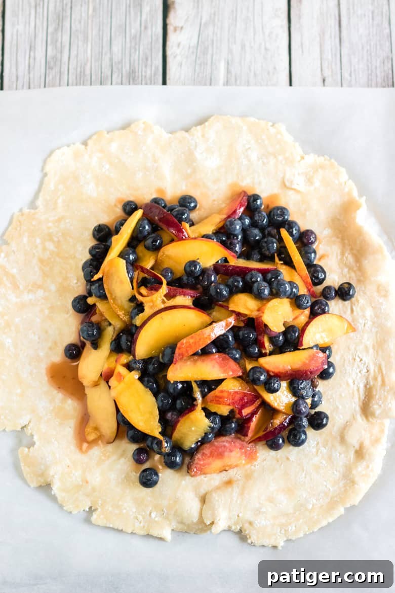 Assembling a peach blueberry galette on parchment paper, with fruit filling centered and dough edges folded over.