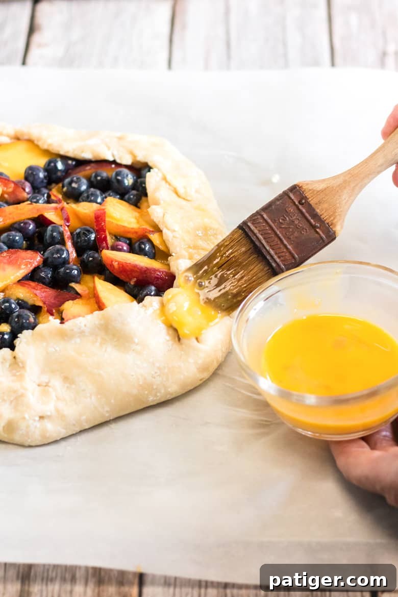 Brushing the folded crust of a peach blueberry galette with an egg wash before baking.