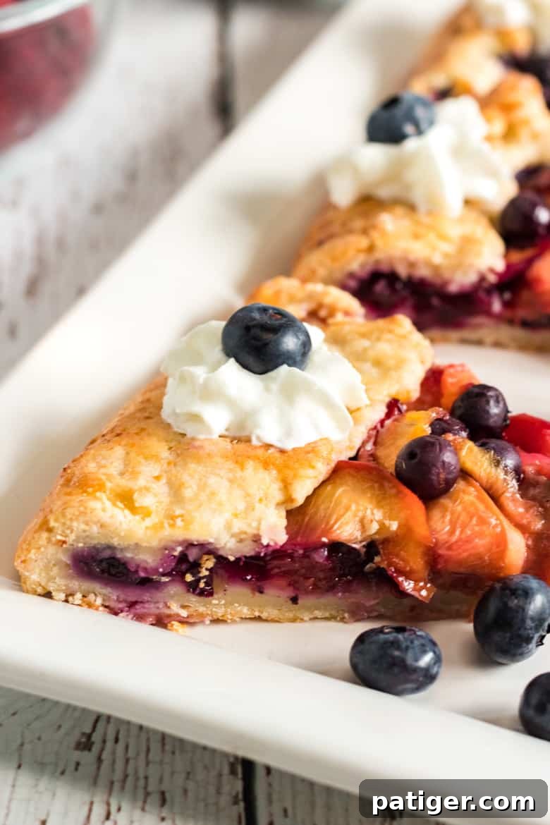 A slice of warm peach blueberry galette topped with a dollop of whipped cream, ready to be enjoyed.