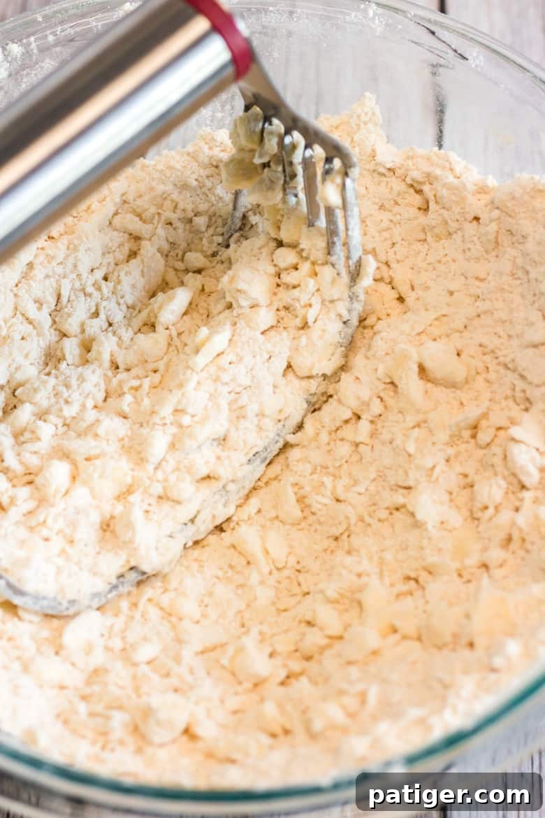 A pastry cutter cutting cold butter into all-purpose flour in a mixing bowl for galette dough.