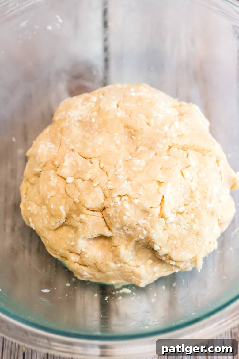 A perfectly shaped ball of galette dough, covered in plastic wrap, ready for chilling.