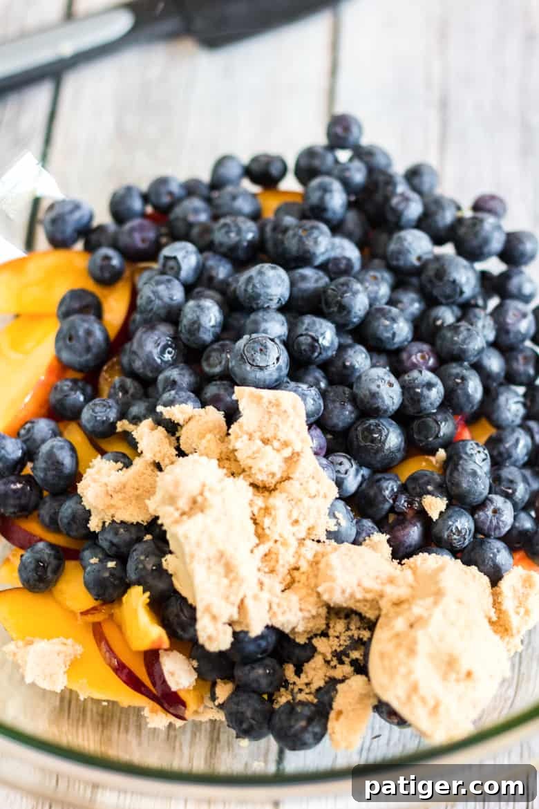 A large bowl filled with sliced peaches and fresh blueberries, coated in brown sugar, cornstarch, and almond extract, ready for assembly.