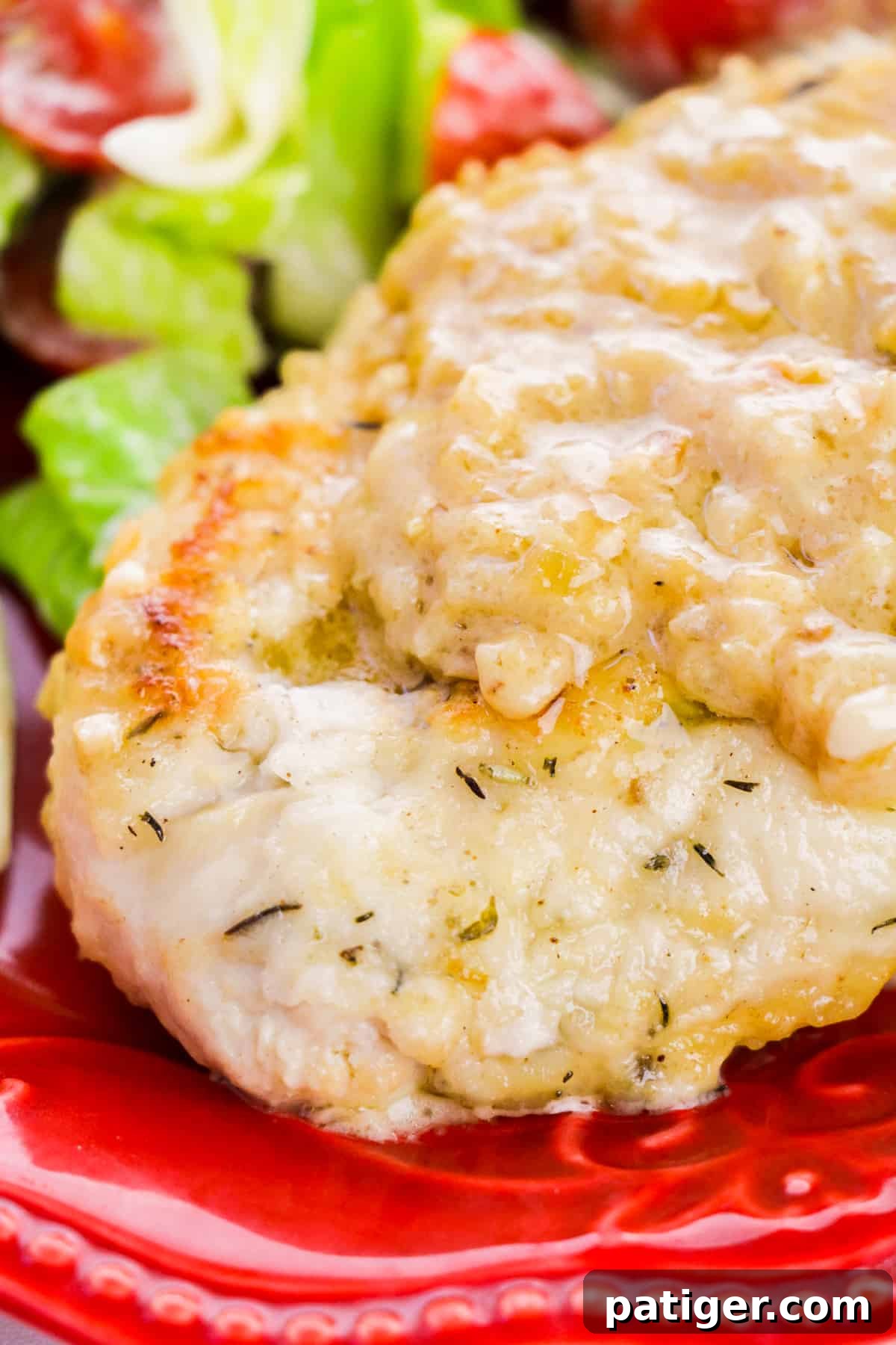 A close-up view of a Smothered Chicken Breast, glistening with gravy, served with a vibrant green salad on a red plate, highlighting its appetizing appeal.