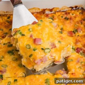 A slice of farmers casserole being lifted from the baking dish, highlighting its chunks of ham, bits of green onion, and golden melted cheese.