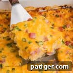 A slice of farmers casserole being lifted from the baking dish, highlighting its chunks of ham, bits of green onion, and golden melted cheese.