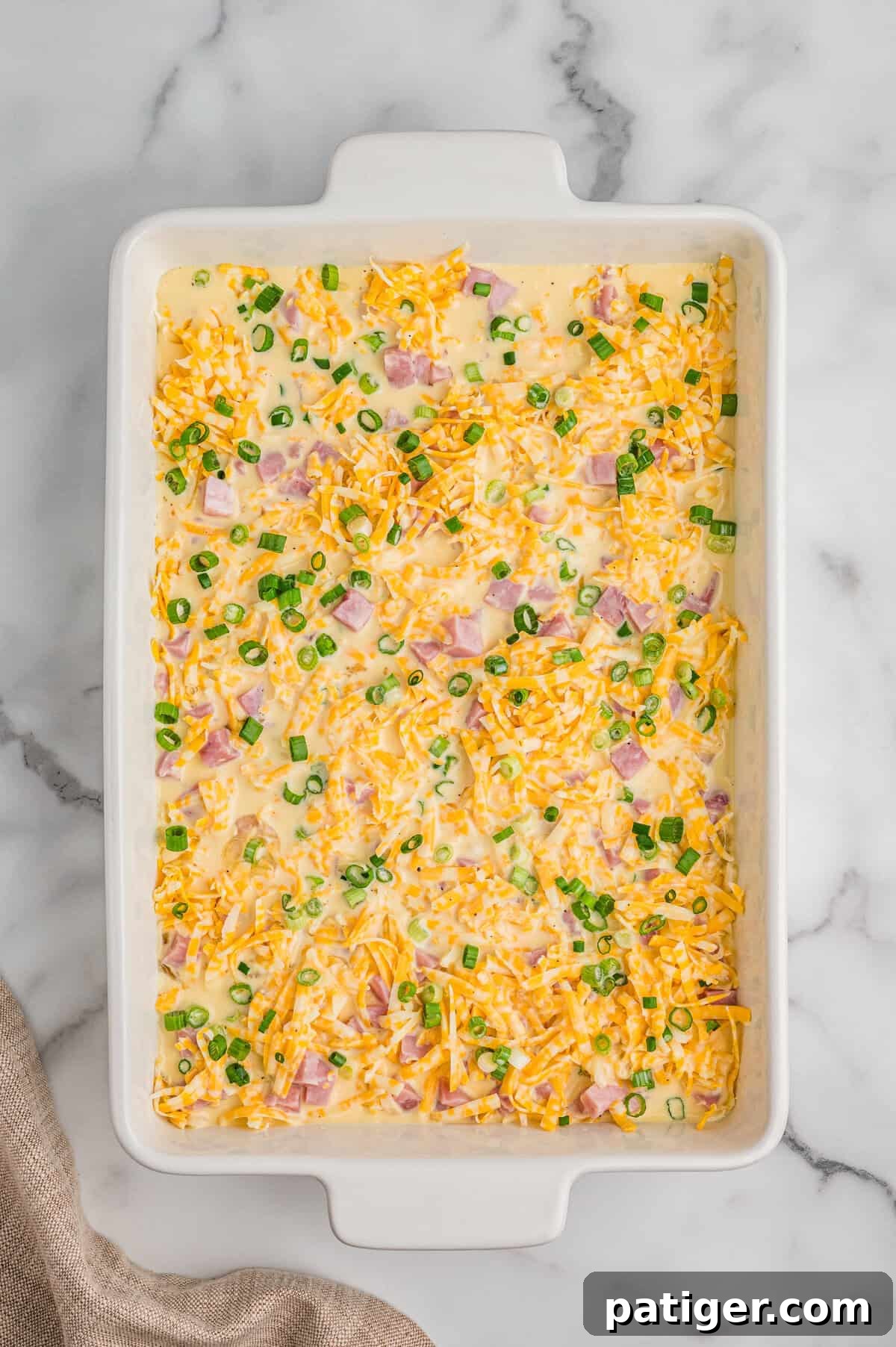 Breakfast casserole ingredients in casserole dish with egg mixture poured over them.