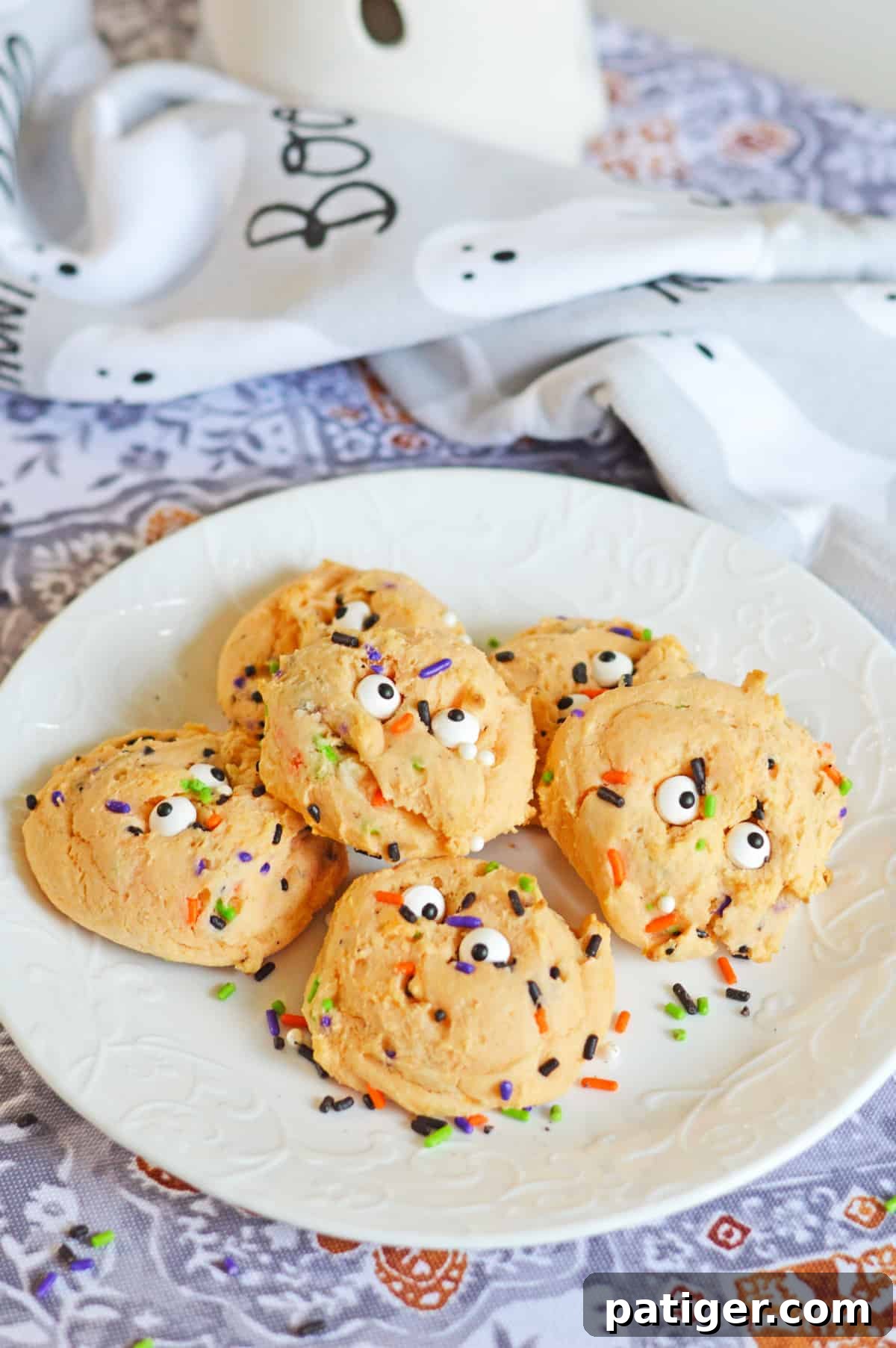 Orange Halloween cookies with sprinkles and eyeballs on a white plate