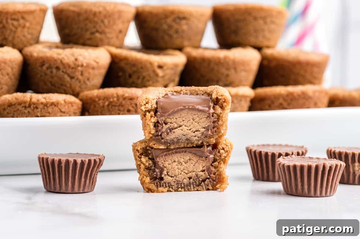 peanut butter cookies with peanut butter cups pressed in center. Several cookies are stacked neatly on platter and one is removed and cut in half to show inside. 