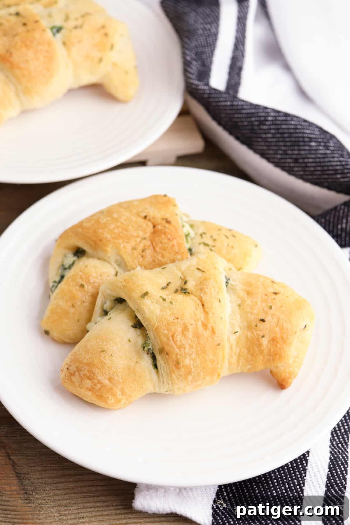 Spinach artichoke crescent rolls on whit plate with another plate of rolls in the background