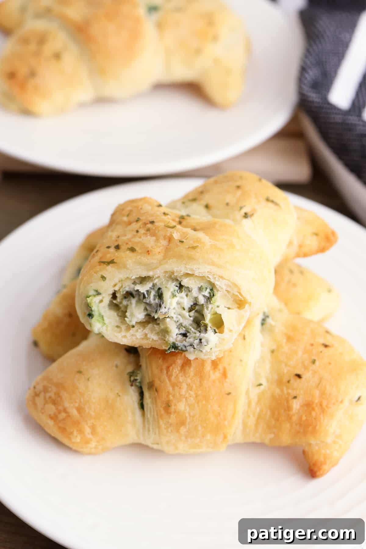 Three spinach artichoke crescent rolls on a plate, one with a bite taken out of it to show the creamy and cheesy spinach dip inside of it.