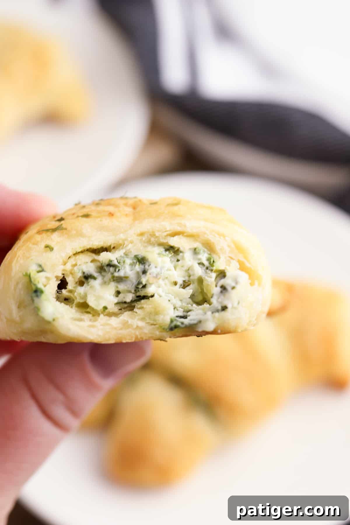 hand holding a spinach dip stuffed crescent roll with a bite taken out of it