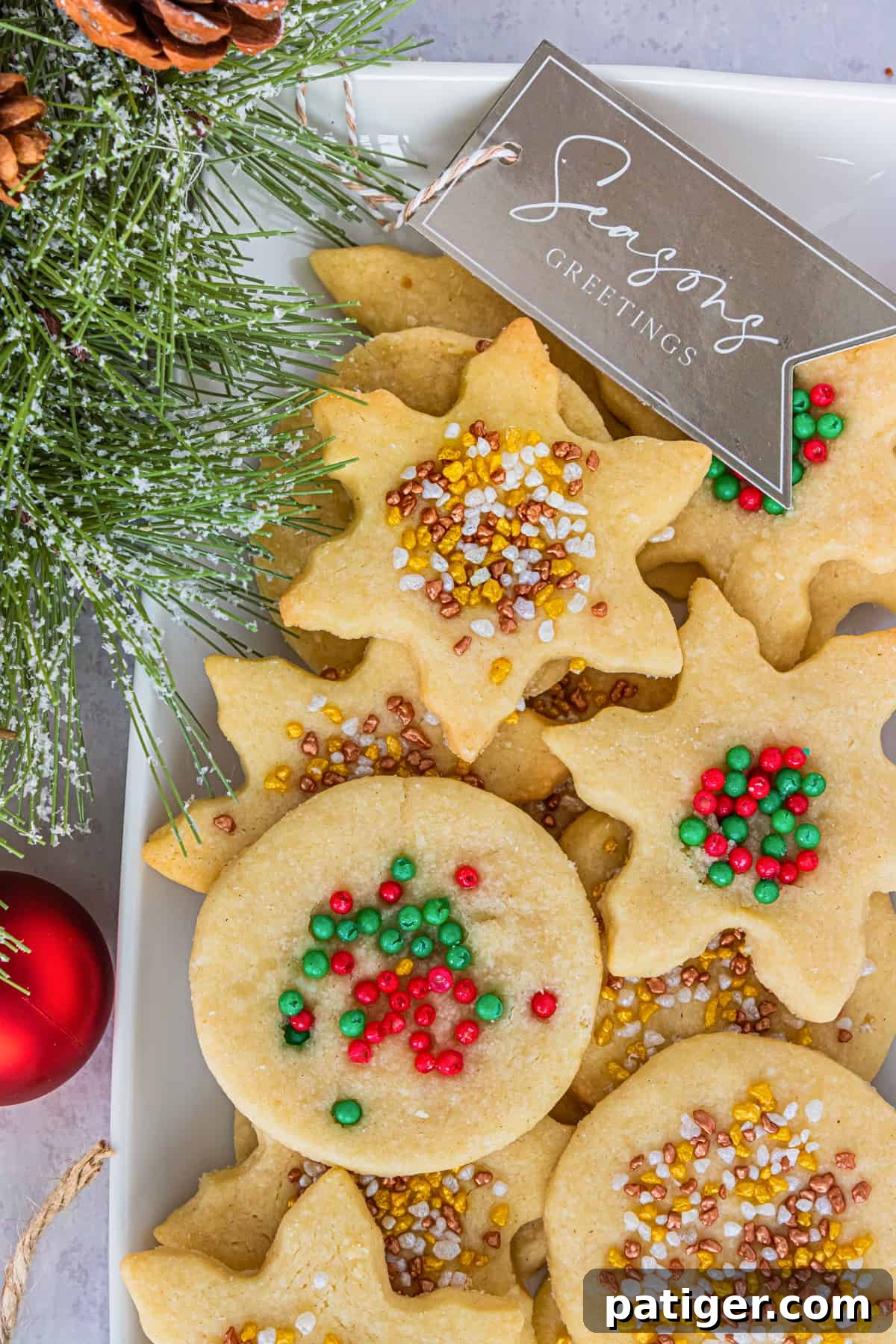 Snowflake and circle-shared shortbread cookies with sprinkles on top served on a white plate next to branch of Christmas tree
