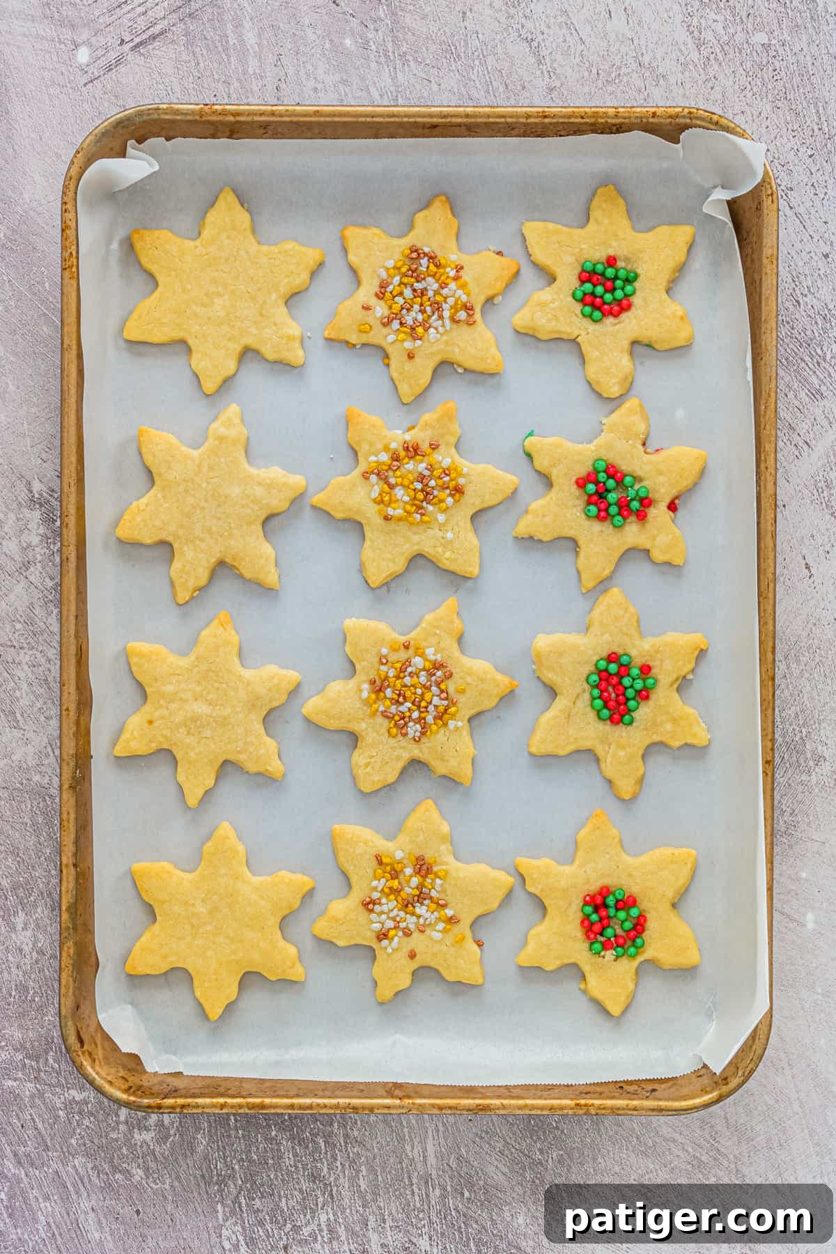 Snowflake Shortbread Cookies on lined baking sheet. Some are topped with sprinkles, others are plain