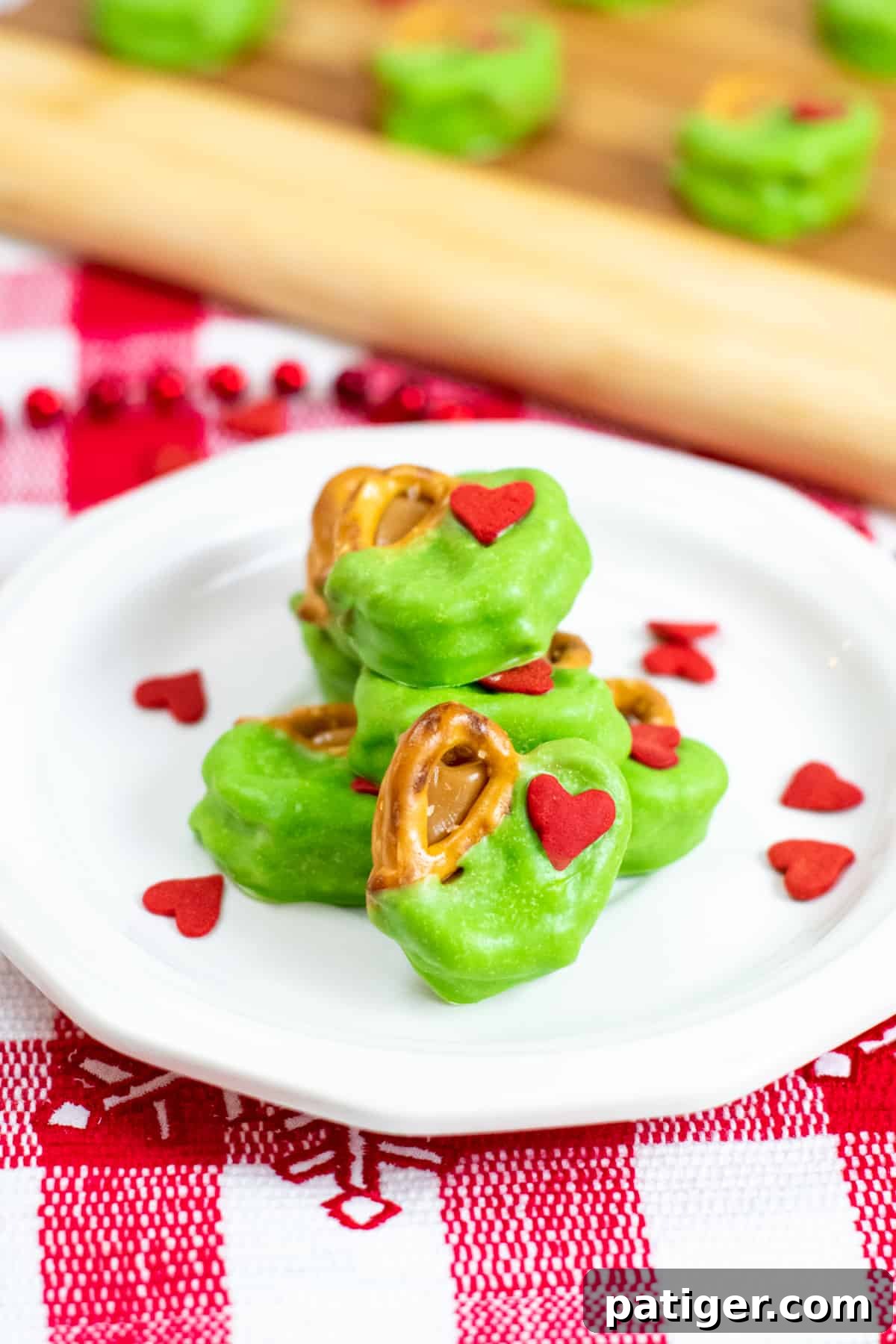 Grinch Pretzel Bites on white plate with red heart sprinkles sprinkled around them
