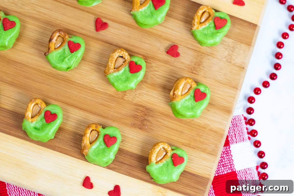 Grinch pretzel caramel bites dipped in green candy and topped with a red heart sprinkle.